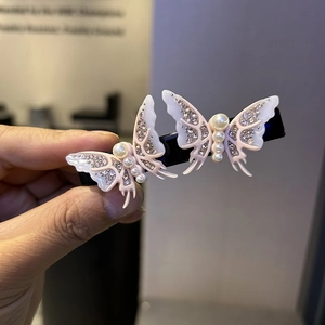Detail of light pink acetate butterfly hair clips with pearls and rhinestones on black clips