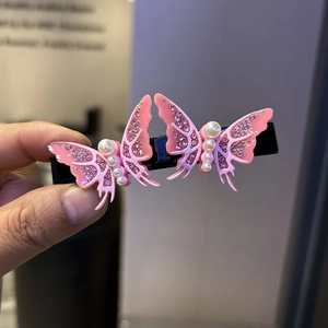 Close-up of pink butterfly hair clip with rhinestones and white pearls on black metal bar