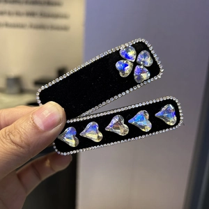 Close-up of black velvet hair clips with rhinestone edges and iridescent heart crystals