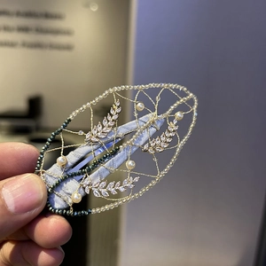 Handmade woven leaf hair clip with pearls and green beads on a gold metal mesh