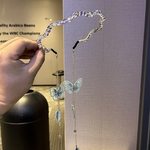 Detail of a wavy rhinestone headband with long fringe chains and blue butterfly embroidery