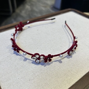Détail d'un serre-tête en velours rouge avec fleurs creuses, perles et strass brillants