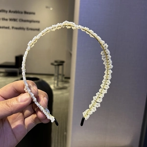 Gros plan de perles blanches tissées à la main sur un serre-tête fin en métal doré
