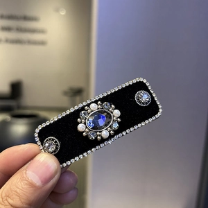 Detail view of velvet hair clip with blue gemstone and white pearl embellishments