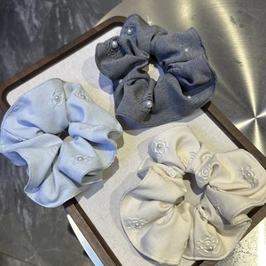Detailed view of three embossed floral pearl scrunchies in grey, blue, and cream on a tray
