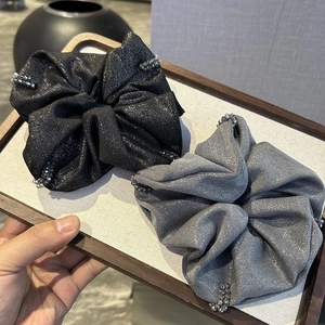 Detailed view of grey and black sparkling scrunchies with elegant bead trim on a wooden base