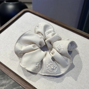 Macro view of cream fabric scrunchie with camellia embroidery and pearl details