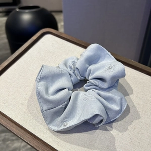 Macro detail of a light blue silk scrunchie featuring white pearls and floral embroidery