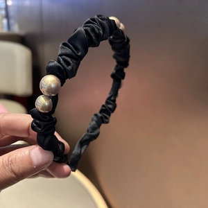 Detail of elegant black pleated satin headband with three large luxury pearls