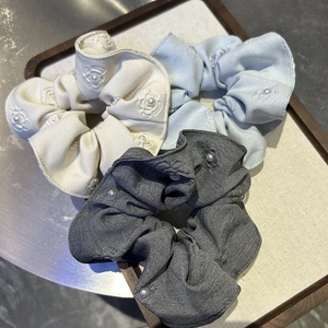 Detail of fabric scrunchies with camellia embroidery and pearls in ivory, blue, and grey