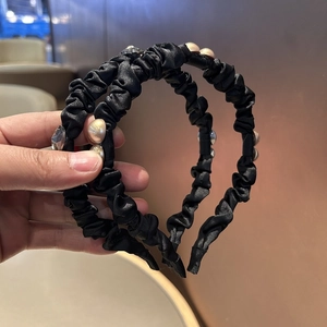 Detail view of black pleated satin headband with champagne pearls and clear crystals
