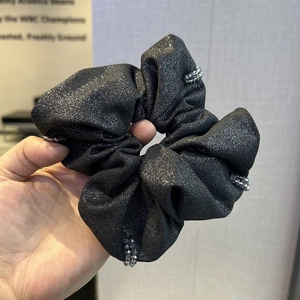 Close-up of a grey beaded scrunchie featuring black glitter fabric and crystal details