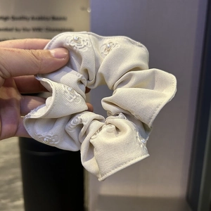 Detail of beige satin scrunchie with pearl embellishments and embroidered pattern