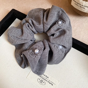 Close-up of gray linen scrunchie with rose embroidery and elegant white pearl accents