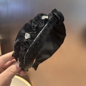 Detail eines schwarzen Satin-Haarreifs mit Herz-Strasssteinen und glitzernder Schmuckkette