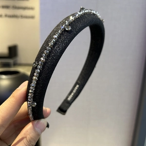 Detail of a black wide headband with grey sparkling rhinestones and handmade label