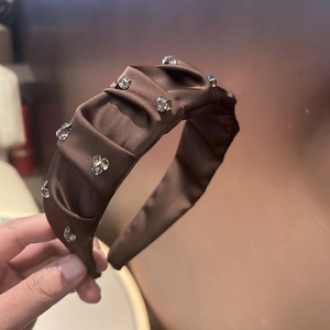 Close-up of elegant dark brown satin headband with sparkling rhinestones and ruched texture