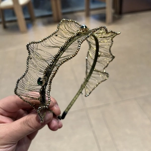 Detailed view of luxury gold mesh headband with intricate beadwork and green crystals