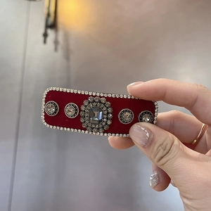 Macro detail of a red velvet hair clip with rhinestone trim and center grey gemstone