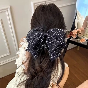 Rear view of a large black polka dot mesh bow hair clip styled on long wavy hair