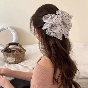 Close-up of a white polka dot mesh bow hair clip styled on long brunette wavy hair