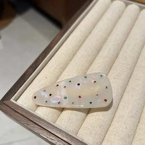 Detail of colorful rhinestones on pearl white acetate duckbill hair clip on wood tray