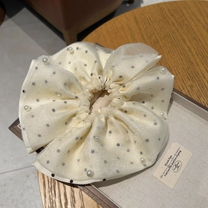 Détail d'un chouchou en maille crème avec pois noirs et élégantes perles décoratives