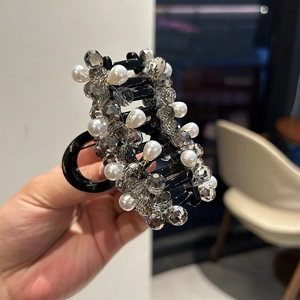 Grande molletta per capelli in resina nera con cristalli grigi e perle bianche vista a mano