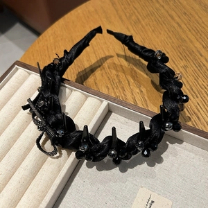 Elegant black silk twisted headband with crystal beads and a bow on a beige velvet box