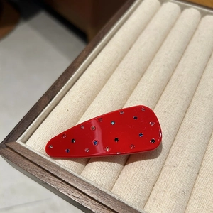 Macro view of a red drop-shaped resin hair clip with colorful scattered rhinestones