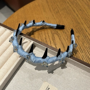 Detail of light blue mesh headband with black rivets and crystal stars on velvet tray
