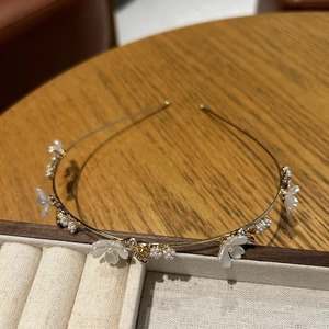Primer plano de una diadema dorada con flores blancas, perlas y pedrería de cristal