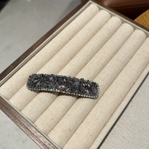 Close-up of luxury rectangular hair clip with dark grey stones and iridescent gems