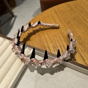Dettaglio di cerchietto in raso rosa con cristalli, perle e punte nere stile punk