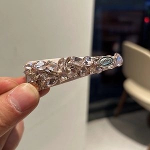 Detailed macro of crystal-embellished duckbill hair clip with pink stones and love metal tag