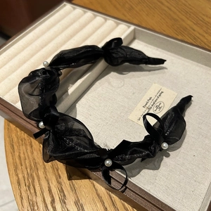 Detail of elegant black mesh headband with white pearl accents on wooden display tray