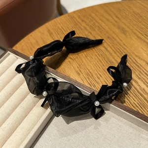 Detail of black mesh headband with satin rosettes and faux pearls on a beige velvet tray