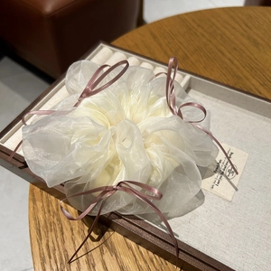White organza scrunchie with pink ribbon bows on a wooden jewelry display tray