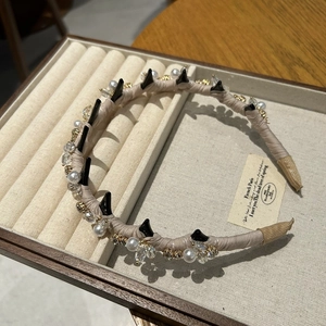 Dettaglio di cerchietto lusso con perle, cristalli e borchie nere su raso beige