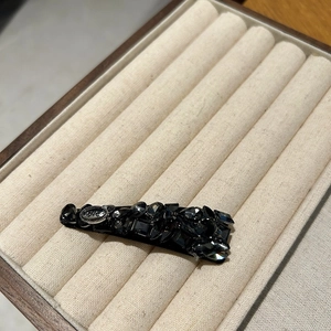 Detailed close-up of a black crystal hair clip with LOVE engraving on a beige tray
