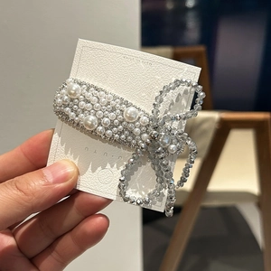 Elegant floral hair clip with white pearls and sparkling crystals on a textured card