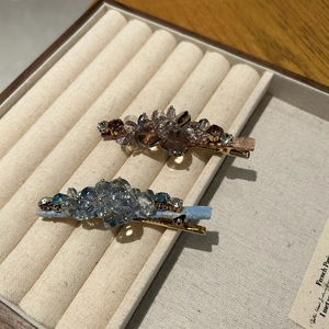 Close-up of crystal flower duckbill hair clips in purple and blue on a soft velvet tray
