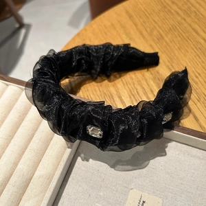 Détail d'un serre-tête en tulle plissé noir avec cristaux posé sur un plateau