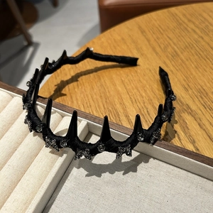 Detail view of black velvet headband with spikes and rhinestone stars on a beige tray