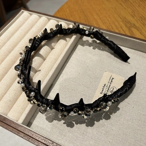 Detailed view of luxury black headband with spikes, crystals and pearls on beige velvet