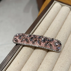 Close-up of pink luxury hair clip with smoke grey rhinestones on beige velvet