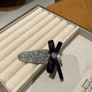Detailed close-up of a luxury crystal rhinestone hair clip with a black ribbon bow detail