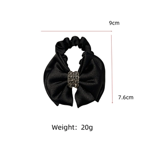 Detail view of a black satin bow hair scrunchie with rhinestones showing 9cm by 7.6cm size