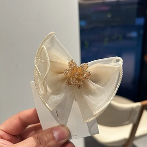 Detailed close-up of layered beige organza bow clip with beaded floral center ornament
