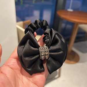 Elegant black satin bow scrunchie with sparkling rhinestone center on hand for daily hairstyle